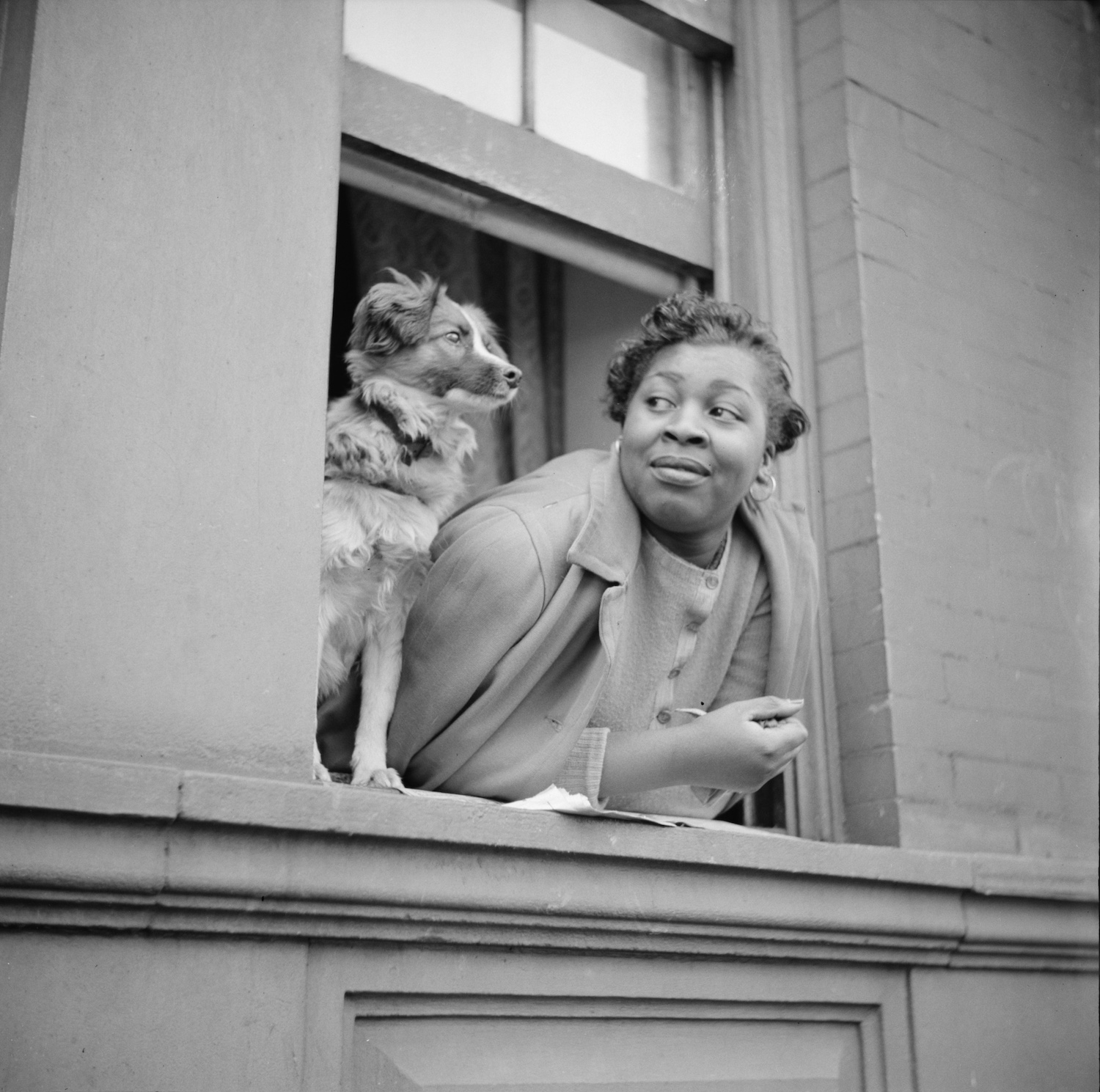 "A Woman and Her Dog in theHarlem Section." A woman looks at her dog, who is looking out the window of an apartment building.